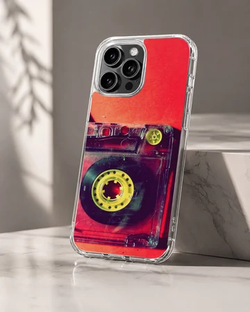 Close-up photograph of a vintage translucent red cassette tape with yellow reels on a phone case — Hero