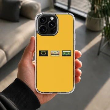 A vibrant yellow phone case featuring three miniature vintage cassette tapes lined up across the center, viewed as a phone case — Lifestyle