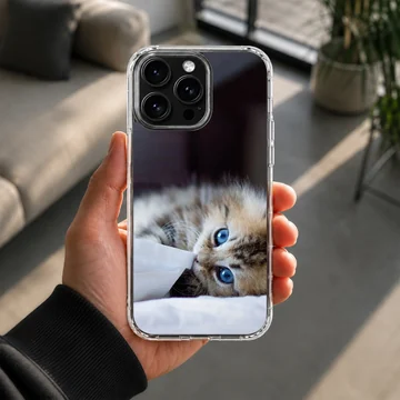 A fluffy kitten with striking blue eyes peeking from under a white blanket on a phone case — Lifestyle