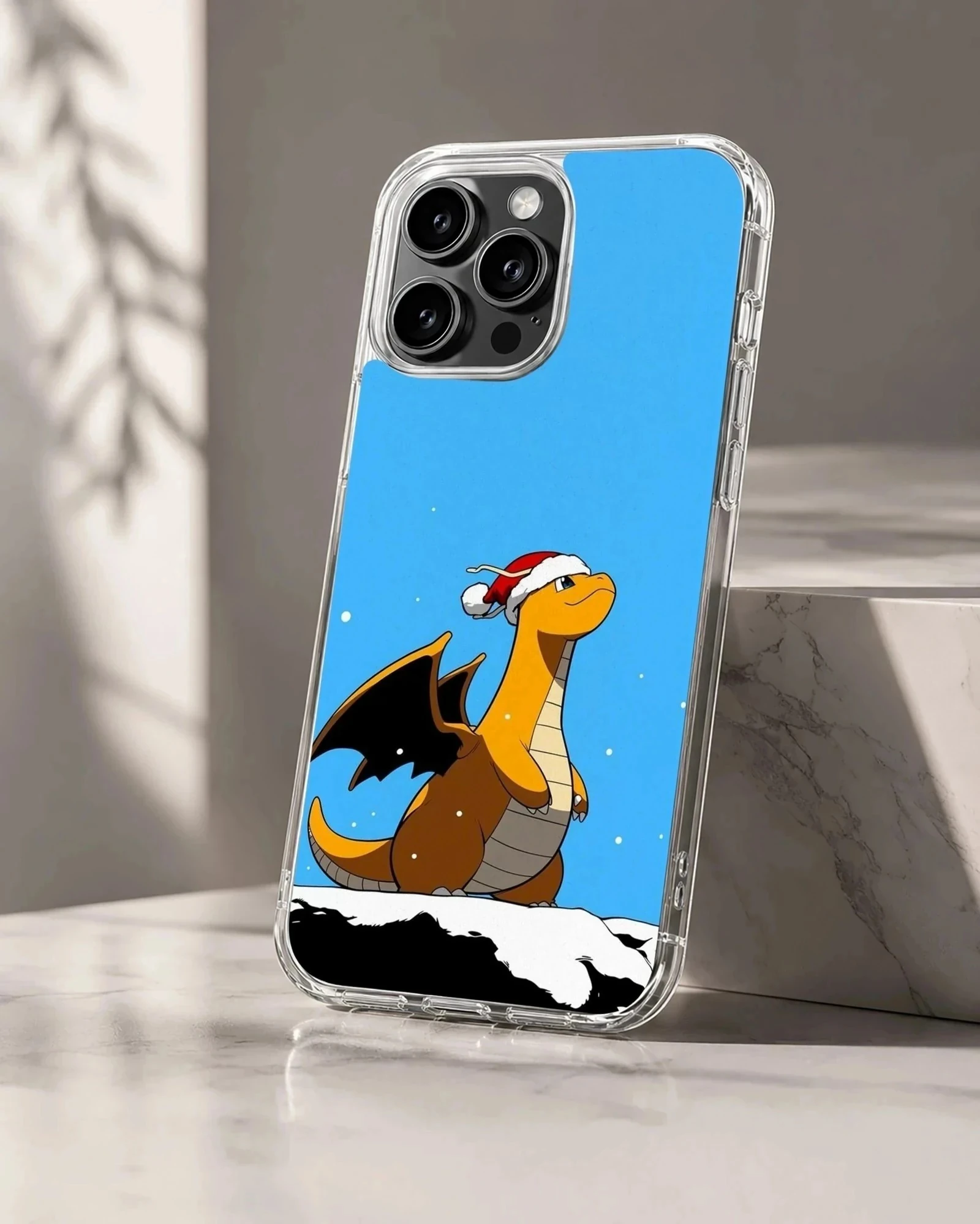 An orange cartoon dragon wearing a Santa hat stands in the snow against a bright blue sky on a phone case