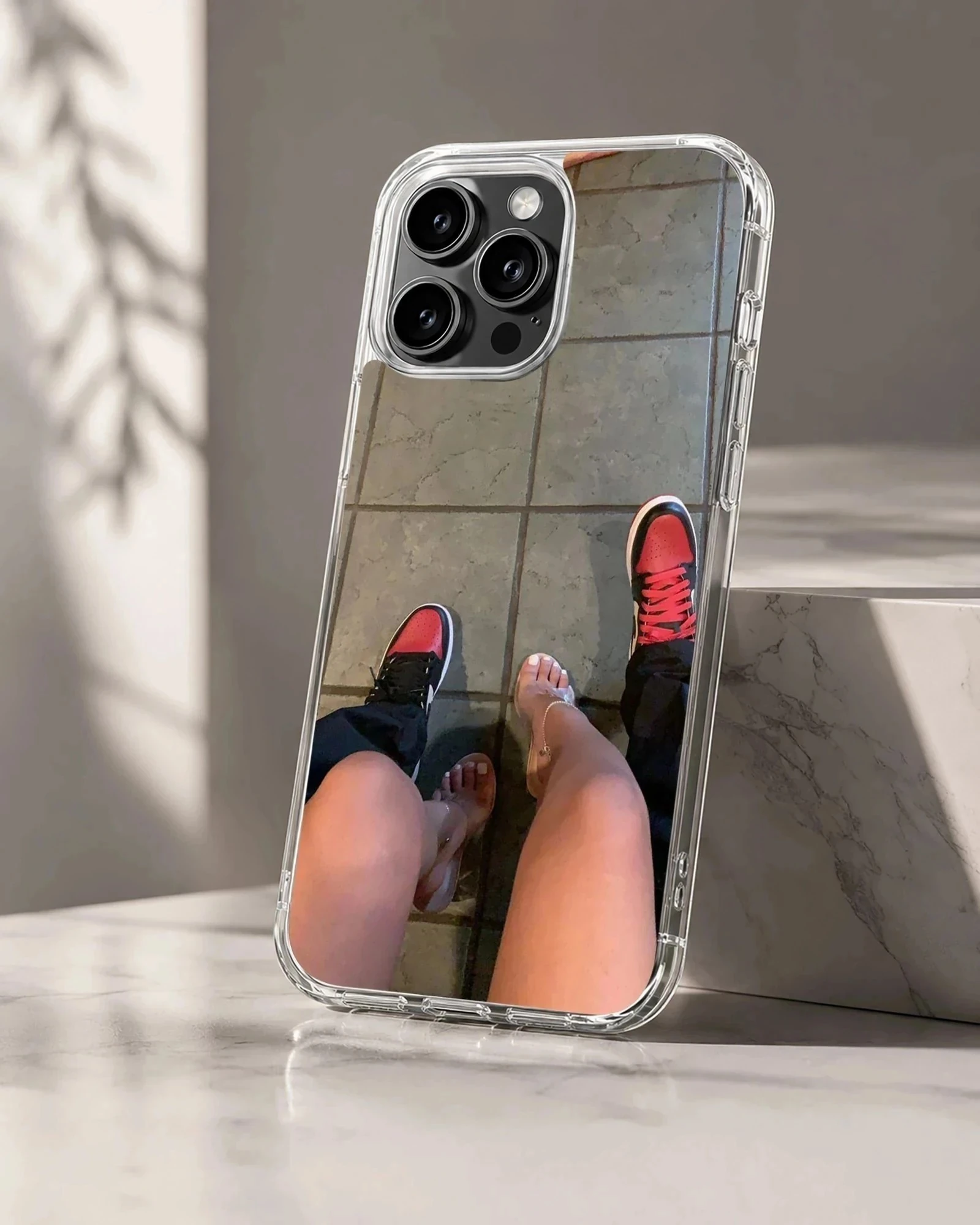 A top-down view of a couple standing together in red sneakers and clear high heels printed on a phone case