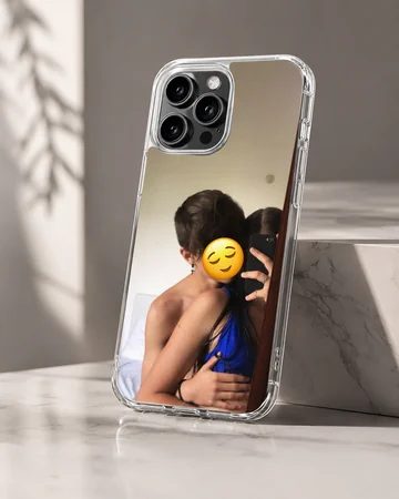 A photograph print on a phone case depicting an embracing couple taking a mirror selfie with a yellow emoji face. — Hero