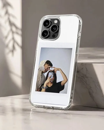 Polaroid-style photo print of a couple making a hand heart during a mirror selfie on a clear phone case.