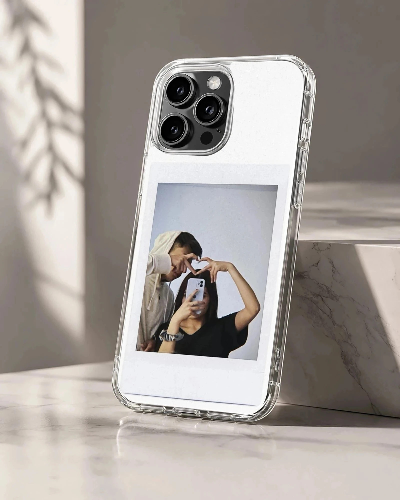 Polaroid-style photo print of a couple making a hand heart during a mirror selfie on a clear phone case.