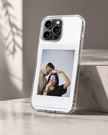 Polaroid-style photo print of a couple making a hand heart during a mirror selfie on a clear phone case. — Hero